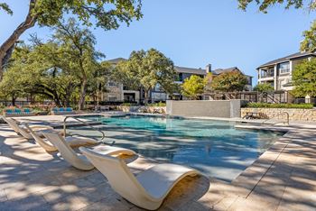 A pool surrounded by lounge chairs and trees.